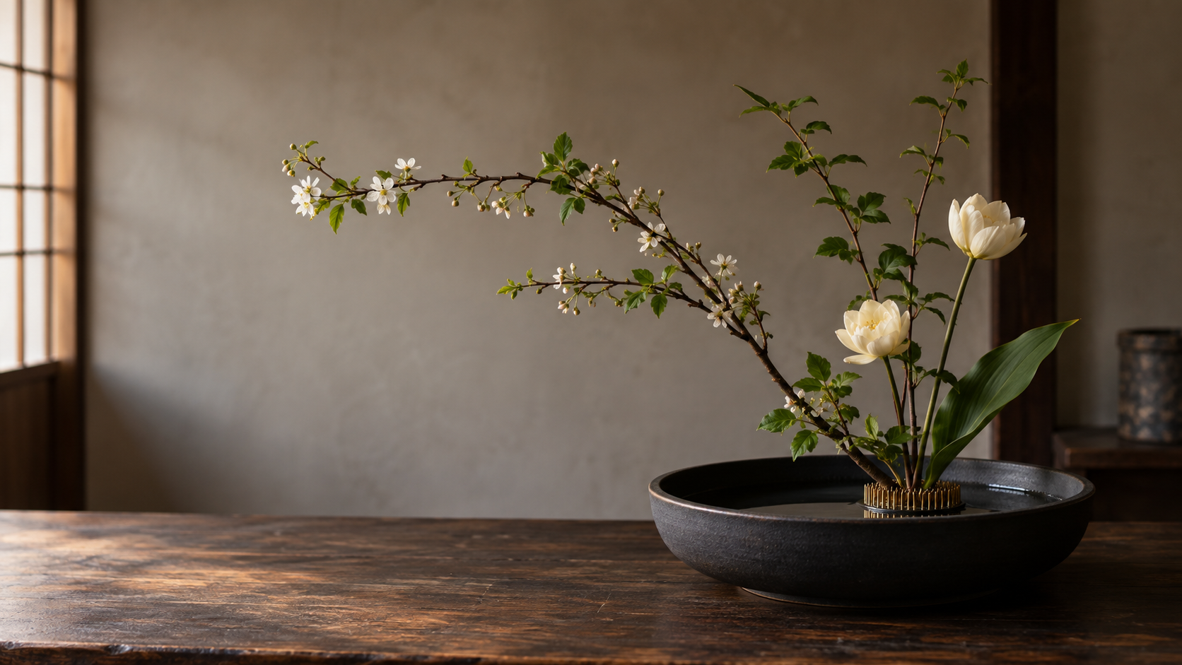 Illustrative ikebana arrangement in a shallow ceramic vessel with a brass kenzan visible beneath the stems
